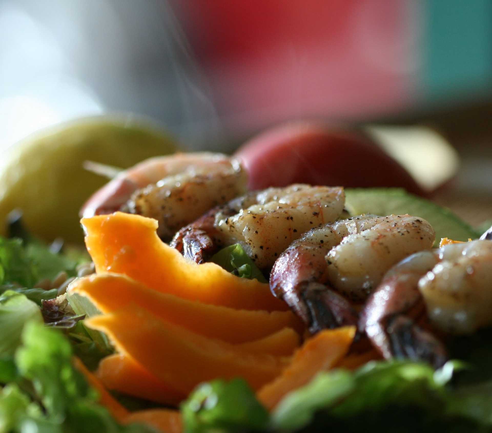 Close-up of a fresh shrimp and mango salad with assorted greens and lemon in the background.